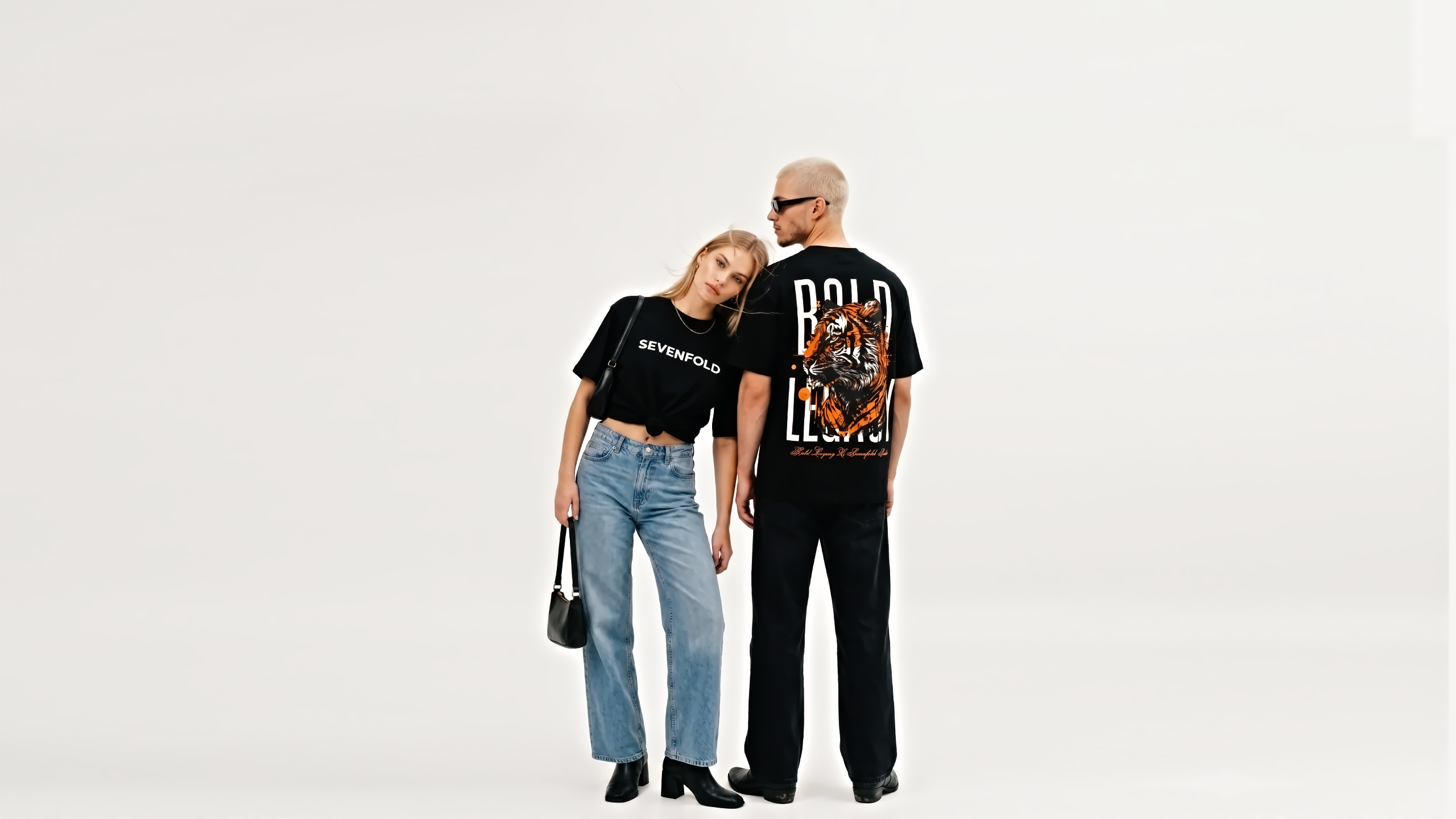 Female model wearing Sevenfold black oversized crop t-shirt with male model in Bold Legacy tiger graphic tee and black wide-leg denim jeans, streetwear fashion studio shoot